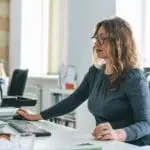 Charming Smiling Adult Woman Middle Aged Woman With Curly Hair Architect Designer Working On Computer In The Bright Modern Office