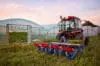 Manual Seedling Planter Mounted To A Tractor In Front Of Greenhouses At Sunset.