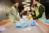 Plastic Trash On Conveyor Near Blurred Multiethnic Workers In High Visibility Vests And Gloves Working Together In Garbage Sorting Center, Garbage Sorting And Recycling Concept