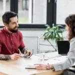 Smiling Account Managers Sitting At Table And Talking In Office