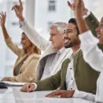Meeting, Seminar And Questions With Business People Hands Raised In The Boardroom During A Strategy Session. Planning, Workshop And A Group Of Colleagues Or Employees Volunteering To Answer At Work