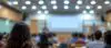 Blurred Background Of Students In Lecture Room With Projector Screen.