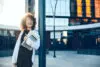 Lovely Curly Haired Entrepreneur With Glasses Smiling Outside While Posing With A Laptop And Tablet