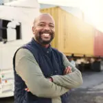 Delivery, Container And Happy Truck Driver Moving Industry Cargo And Freight At A Shipping Supply Chain Or Warehouse. Smile, Industrial And Black Man Ready To Transport Ecommerce Trade Goods Or Stock
