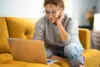 Female Sitting On A Yellow Couch Using Laptop And Internet Conne