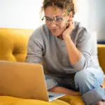 Female Sitting On A Yellow Couch Using Laptop And Internet Conne