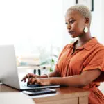 Typing, Online And Black Woman With Laptop, Serious And Thinking Of Ideas In Office And Copywriting. Writer, Working And Creative For Website On Desk, Reading And Confident In Company And Person
