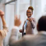 Happy Black Business Seminar Speaker Pointing At Attendee Who Wants To Ask Question In Conference Room.