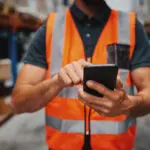 Closeup Of Man Hands Using Mobile Phone While In Warehouse In Uniform