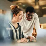 Portrait Of Two Creative Colleagues Using Laptop To Discuss Work