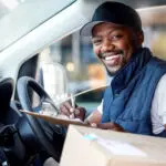 Delivery Man, Transport And Portrait Of A Man Writing With A Smile In Window For Shipping Or Courier Service. Happy Black Person Or Driver With Cardboard Package To Sign Paper In Van Or Cargo Vehicle