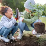 High Five, Child And Woman With Plant For Gardening At Park With Trees In Nature Garden Environment. Happy Volunteer Family Planting For Growth, Ecology And Sustainability For Community On Earth Day
