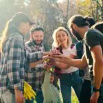Caucasian Team Of Males And Females, Volunteers With Child Putting Hand On Hand In Circle And Making Gesture Of Cooperation And Coworking. Successful Work Together Concept. Eco Activists. Outdoors.