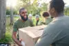 Community Service, Black Man And Giving Box In Park Of Donation, Volunteering Or Social Responsibility. Happy Guy, Ngo Workers And Helping With Package Outdoor Of Charity, Support Or Society Outreach