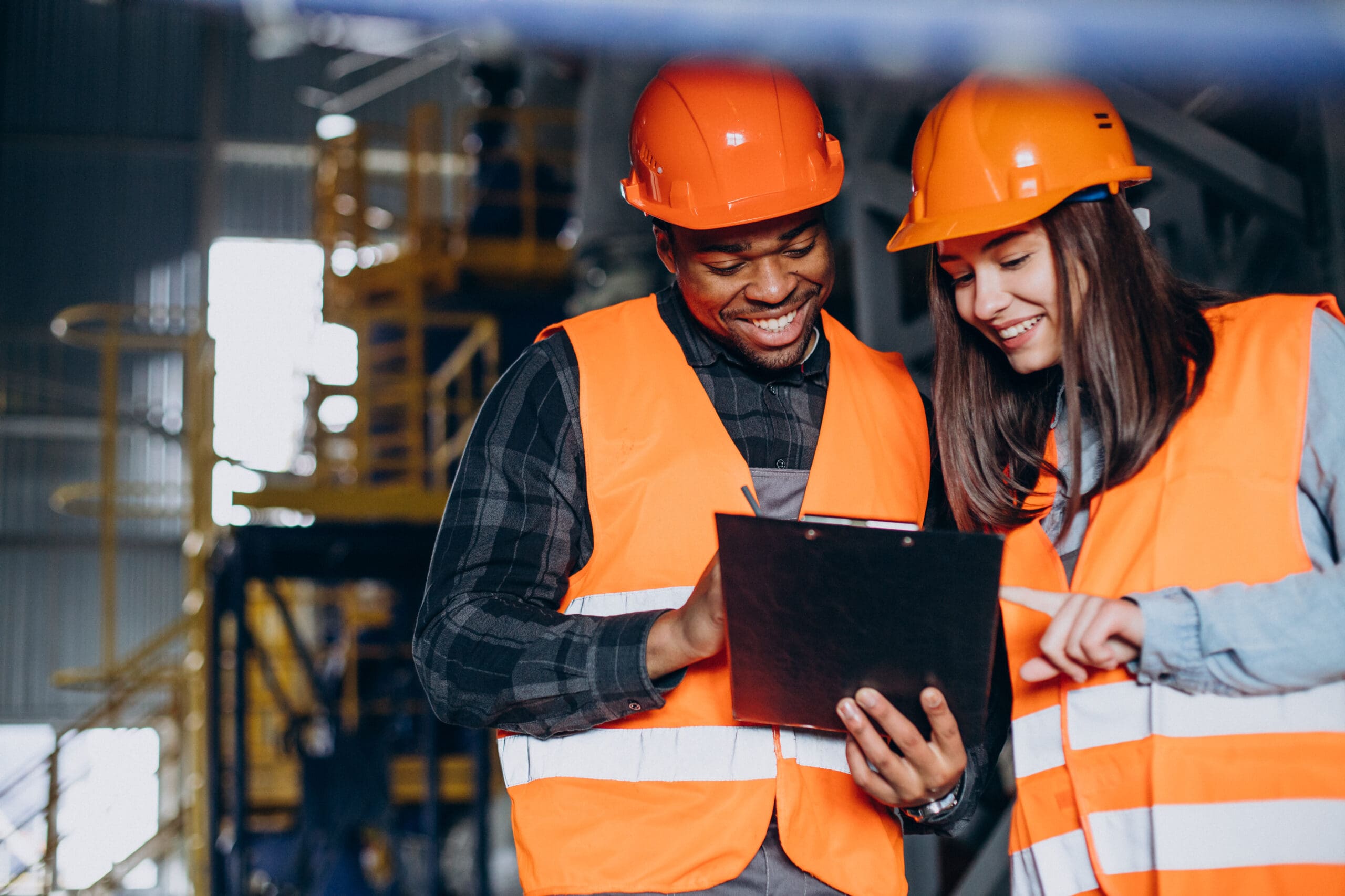 Three Factory Workers In Safety Hats Discussing Manufacture Plan