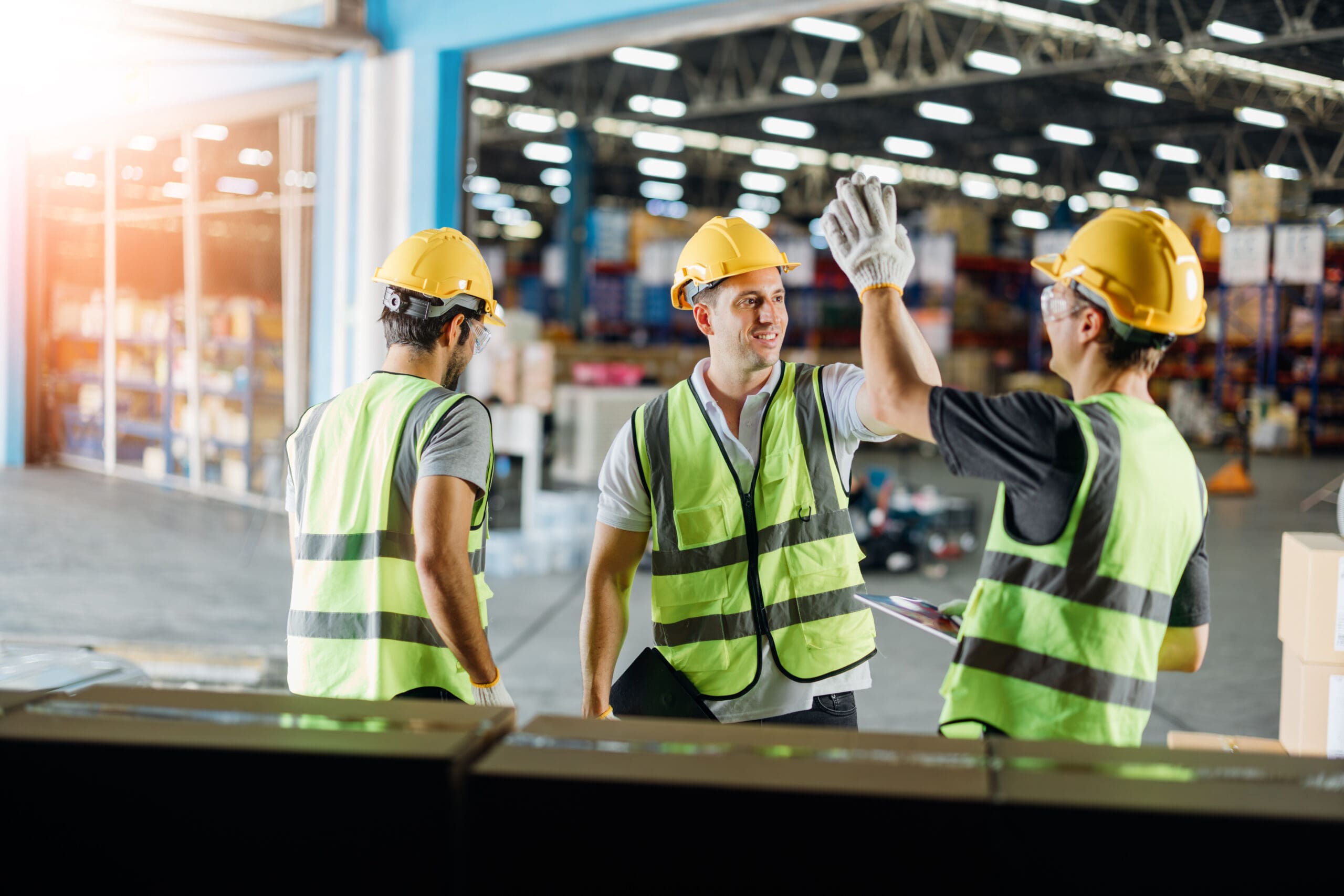 Three Warehouse Workers Using A Digital Tablet While Recording Inventory. Logistics Employees Working With Warehouse Management Software In A Large Distribution Centre.